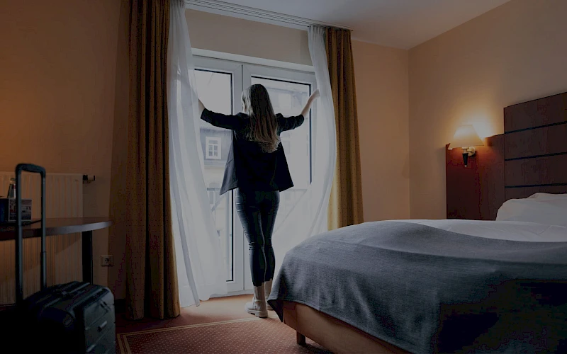 Frau öffnet die luftigen Voile-Vorhangschals eines modernen Hotelzimmers im Hotel Fulda Mitte